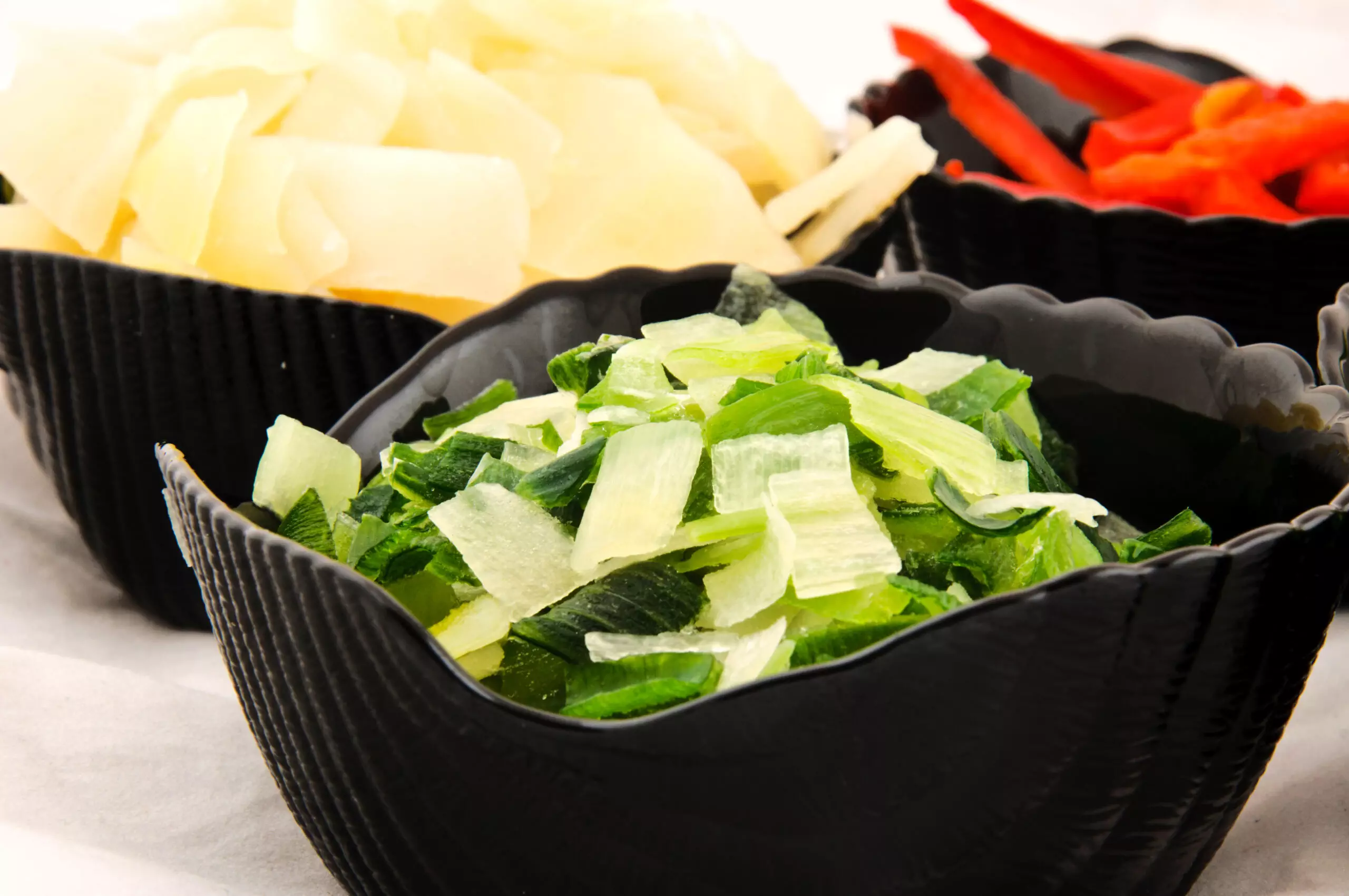 Assorted fresh vegetable slices in black bowls.