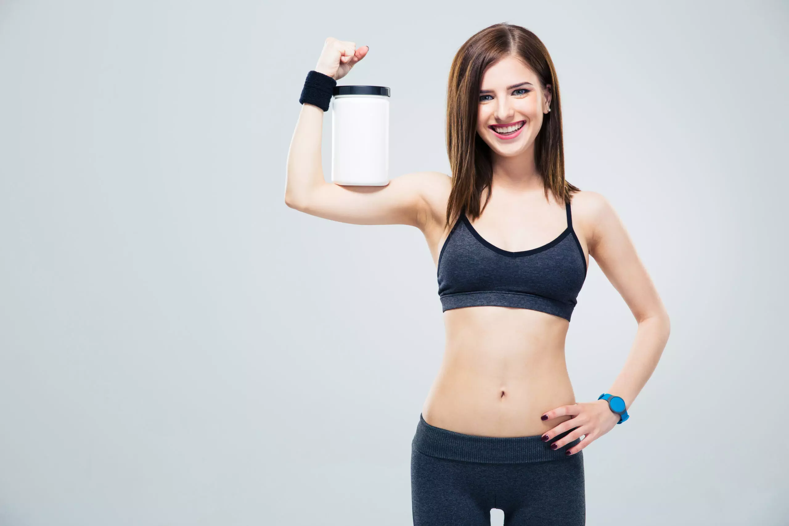 Woman holding protein powder container, fitness attire.